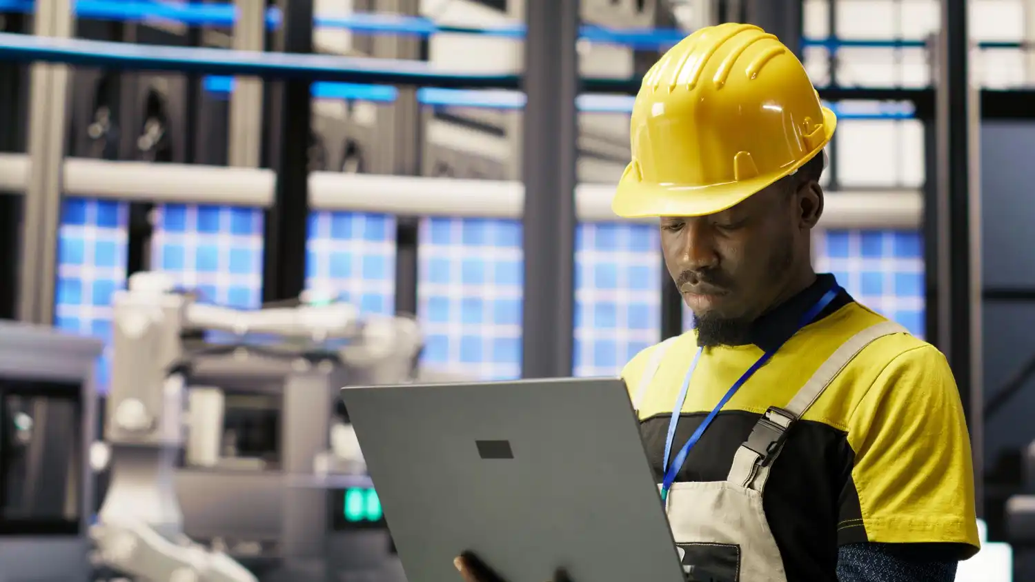 Homem trabalhando em uma fábrica moderna, usando capacete de segurança e analisando dados em um laptop, simbolizando fusões e aquisições como vetor de modernização industrial.